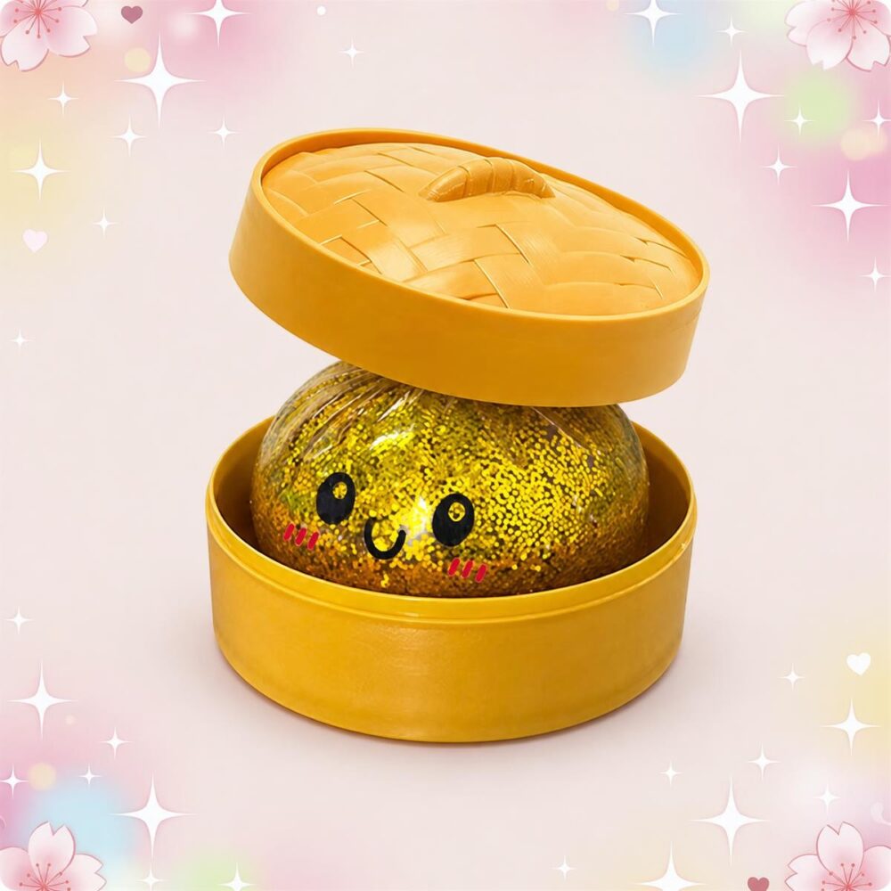 Un anti-stress squishy dumpling scintillant doré, ouvert dans sa boîte ronde jaune, avec un petit visage souriant et un fond rose décoré d’étoiles.