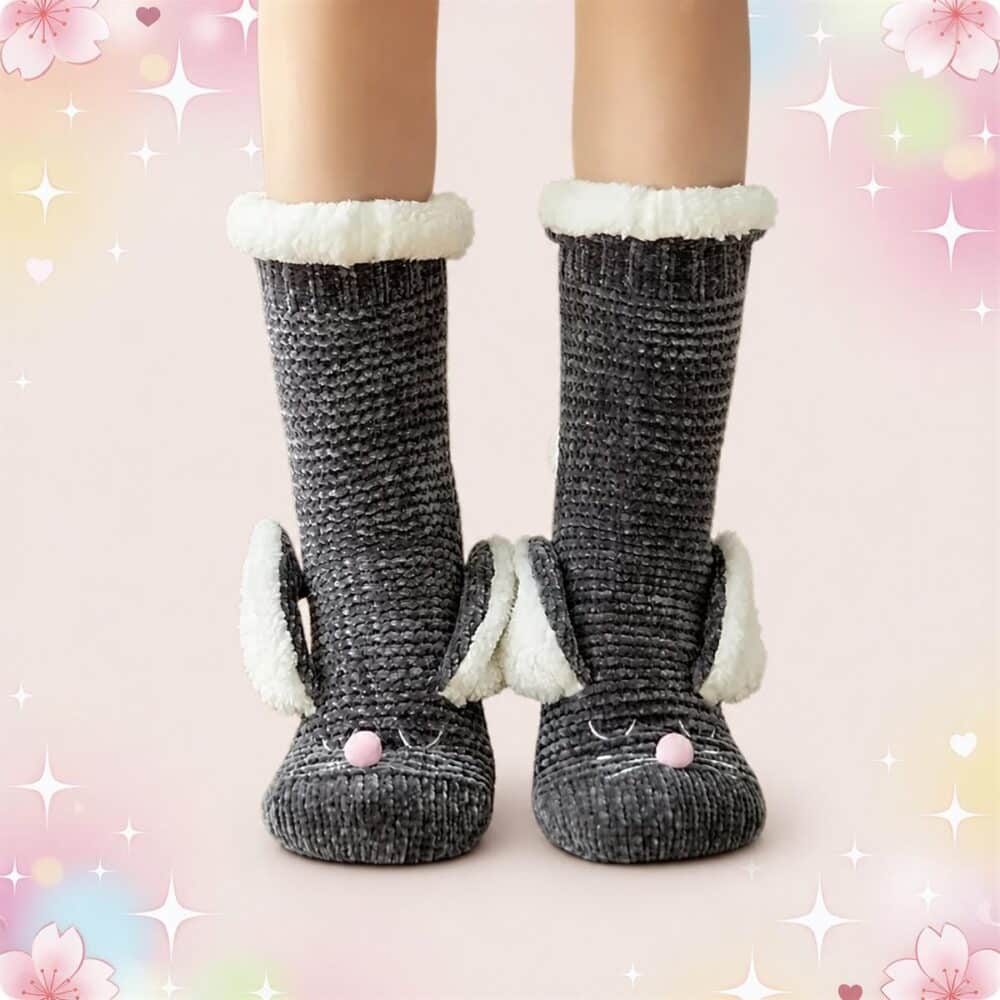Une paire de chaussettes kawaii lapin pour l'hiver grises, avec bordure blanche douce et petite truffe rose, portées aux pieds sur un fond rose pastel décoré d’étoiles et de fleurs.