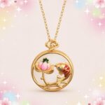 Un collier japonais avec pendentif lotus et Carpe Koï doré, avec un médaillon rond montrant une fleur de lotus rose et un poisson rouge sur fond pastel.