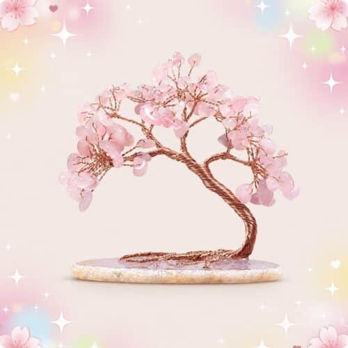 Une décoration cerisier en fleur en quartz rose avec un petit arbre en pierres roses et tronc en fil cuivré, posé sur un socle ovale, sur fond pastel brillant.