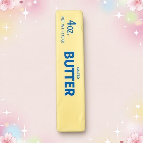 Un jouet anti-stress squishy brique de beurre salé jaune en forme de bloc, posé sur un fond rose pastel décoré de petites étoiles et fleurs.