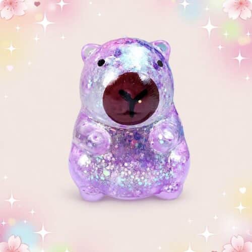 Un Jouet anti-stress squishy Capybara pailleté violet, en forme de petit animal rond et brillant, posé sur un fond rose pastel avec des étoiles scintillantes.