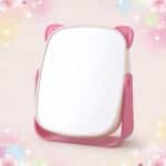 Un miroir kawaii rose pliable à oreilles de chat rotatif, posé sur un fond pastel décoré de petites étoiles et de cœurs.