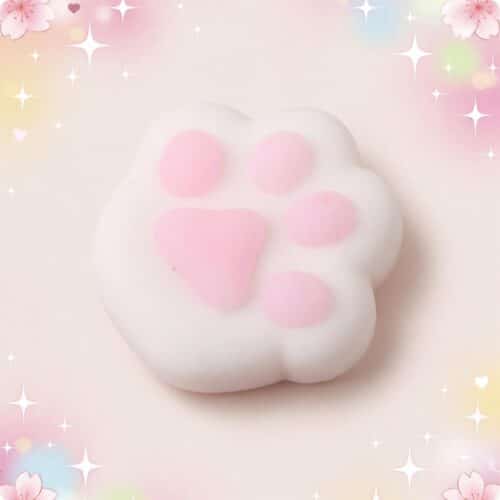 Un mochi squishy anti-stress en forme de patte de chat blanc et rose, tout doux à presser, sur un fond pastel décoré d’étoiles brillantes.