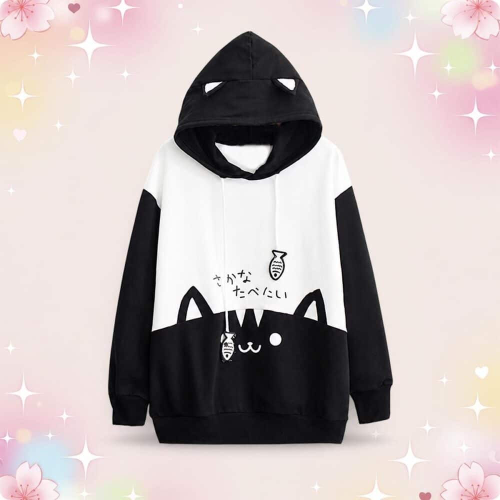 Un Pull kawaii chat et liens poissons noir et blanc, avec capuche à oreilles de chat et petits dessins mignons, sur fond rose pastel avec étoiles scintillantes.