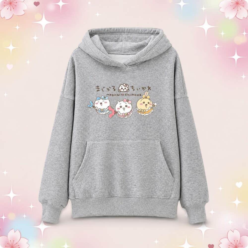 Un pull kawaii Magical Chiikawa gris à capuche avec poche kangourou, décoré de petits personnages mignons, posé sur un fond rose pastel avec des étoiles brillantes.