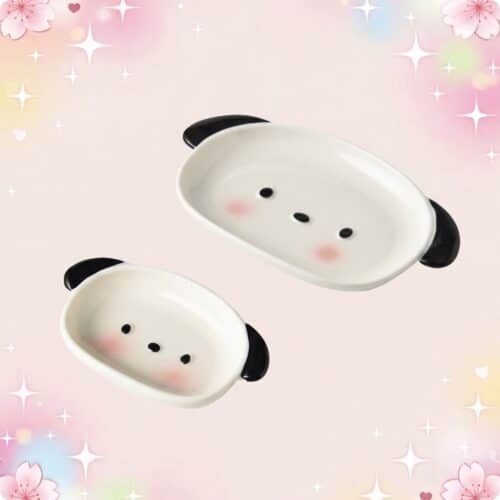 Deux petites assiettes de vaisselle kawaii assiette chiot mignon en forme de visage de chiot, avec des oreilles noires et des joues roses, sur un fond pastel rempli d’étoiles et de fleurs.