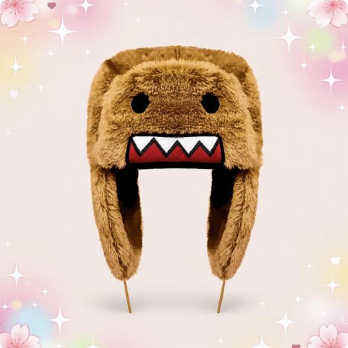 Un bonnet kawaii Domo Kun en fourrure à oreillettes marron, avec des yeux noirs et une bouche dentée, posé sur fond rose pastel décoré d’étoiles et de petites fleurs.