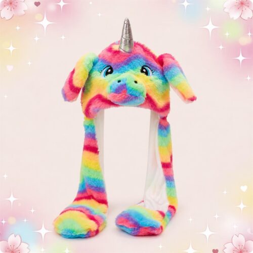 Un bonnet Kawaii licorne multicolore avec corne argentée, tout doux et coloré, avec deux longues pattes pendantes, sur un fond rose pastel avec des étoiles scintillantes.