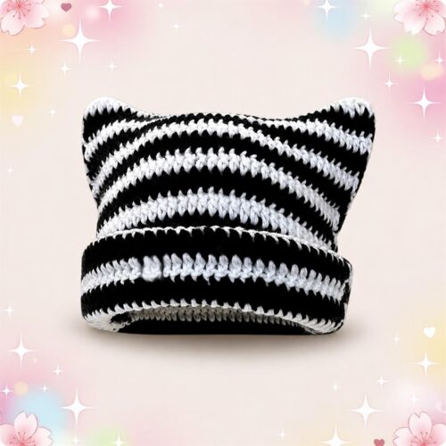 Un bonnet Kawaii à oreilles de chat au motif rayé noir et blanc, en tricot doux, posé sur un fond rose décoré de petites étoiles et fleurs.
