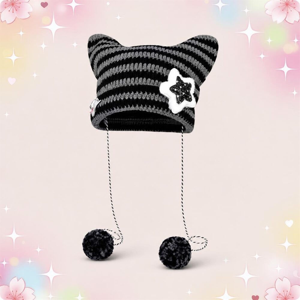 Un bonnet kawaii oreilles de chat rayé à pompons noir et gris, avec deux oreilles pointues, un badge étoile et deux cordons finis par des pompons, sur fond rose décoré de petites étoiles.