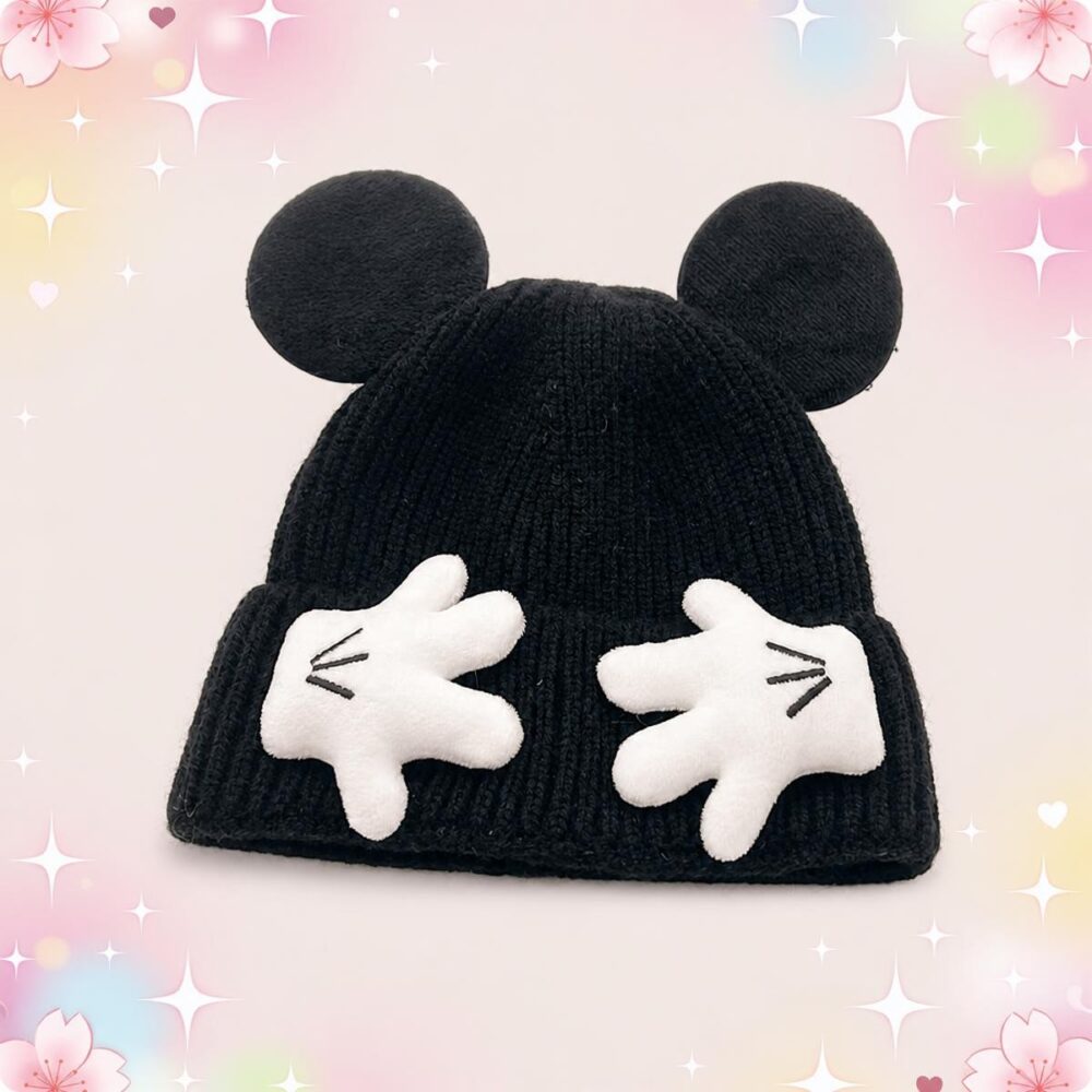 Un bonnet kawaii tricoté à oreilles et mains de souris noir, posé sur un fond rose pastel avec des étoiles brillantes.