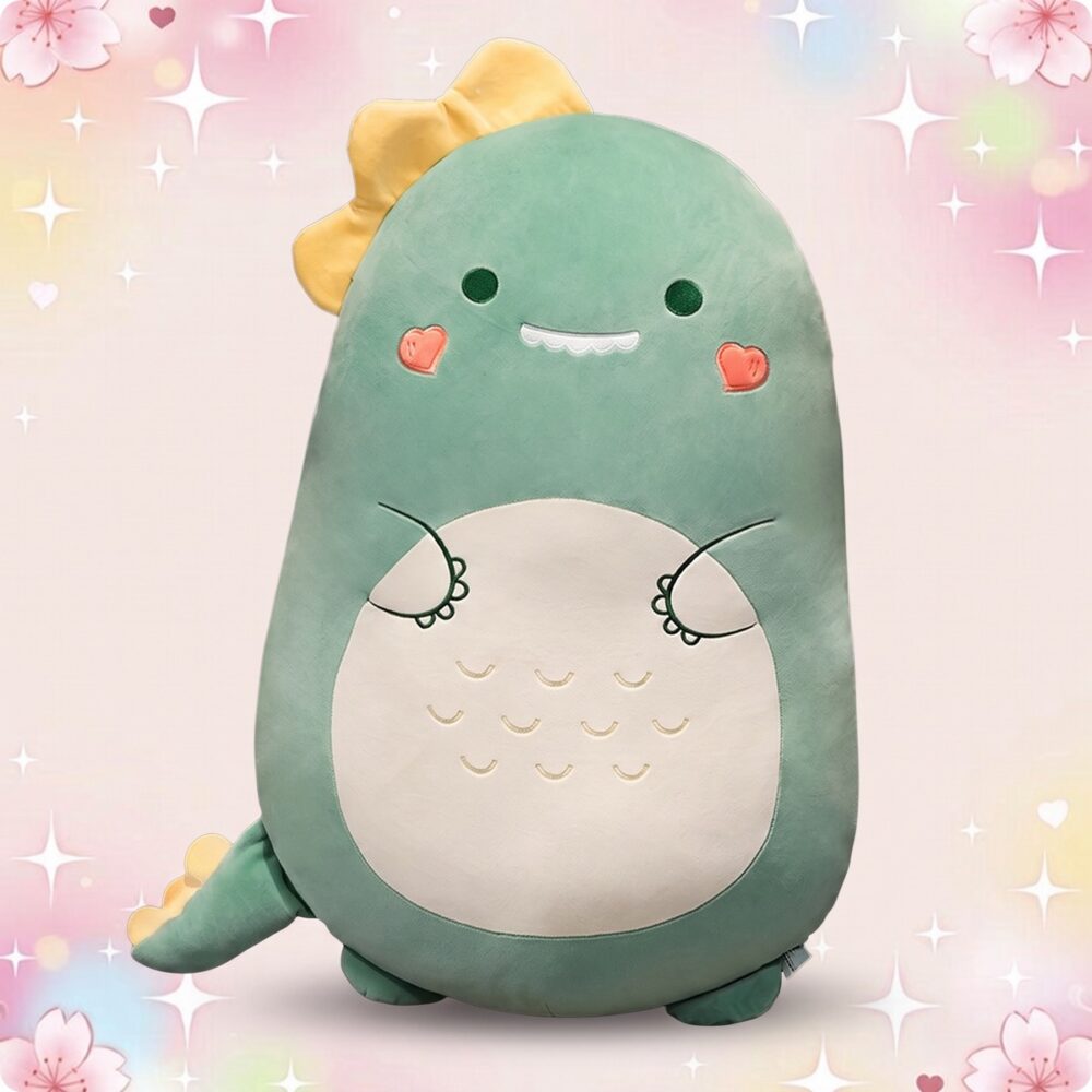 Un oreiller peluche dinosaure vert en forme de petit dinosaure souriant, avec ventre blanc, joues roses et fond pastel scintillant.