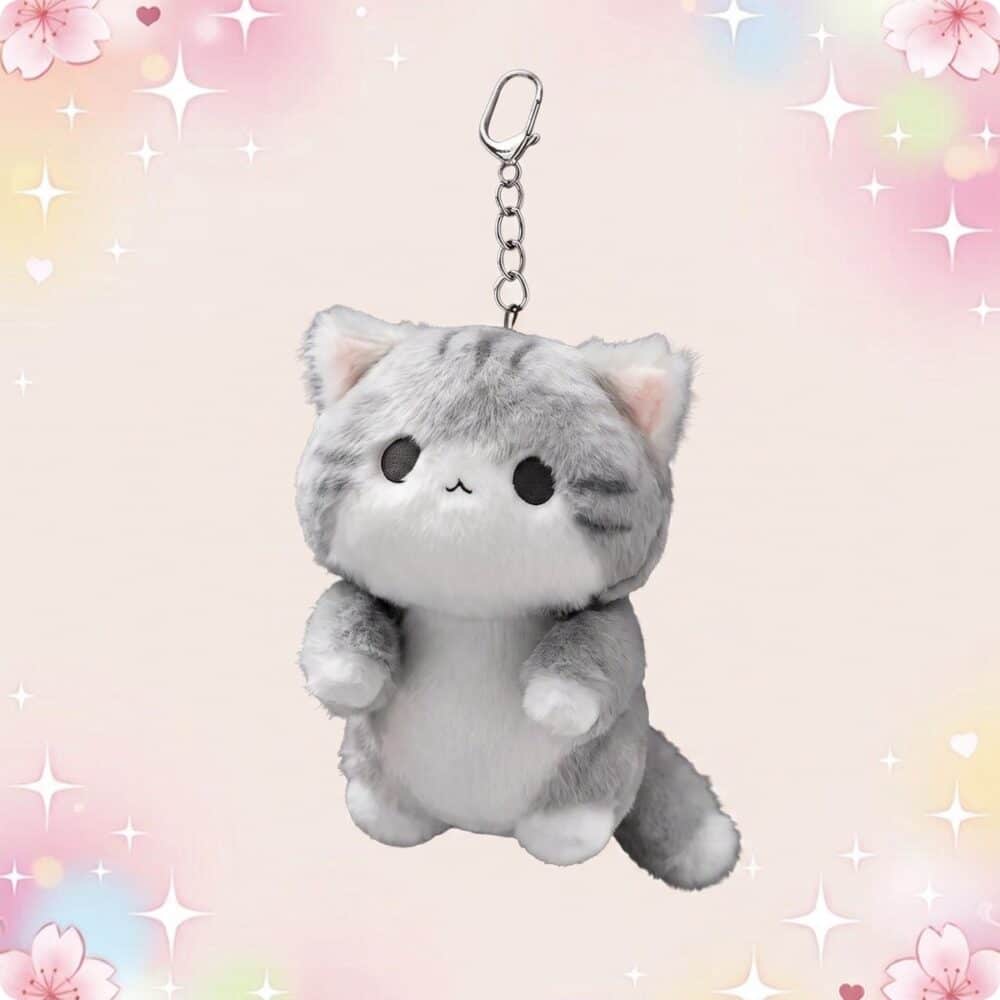 Un porte-clef peluche chat kawaii gris et blanc, en forme de petit chat tout doux avec une chaîne métallique, sur fond pastel décoré d’étoiles et de fleurs.