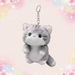Un porte-clef peluche chat kawaii gris et blanc, en forme de petit chat tout doux avec une chaîne métallique, sur fond pastel décoré d’étoiles et de fleurs.
