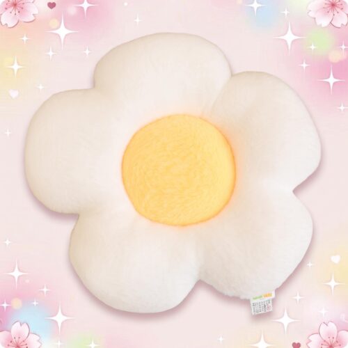 Un coussin kawaii marguerite tout doux, en forme de fleur blanche avec un centre jaune, posé sur un fond rose pastel avec des étoiles et des petites fleurs.