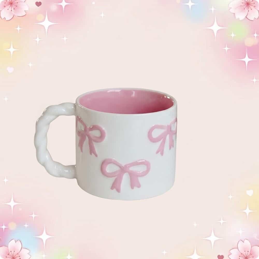 Une tasse kawaii à noeuds roses et anse torsadée blanche, avec intérieur rose, posée sur un fond pastel brillant avec des petits cœurs et étoiles.