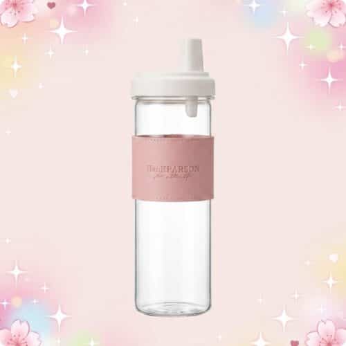 Une Gourde kawaii élégante avec paille intégrée en verre, avec bouchon blanc et bande rose, sur un fond rose pastel avec des fleurs et des étoiles brillantes.