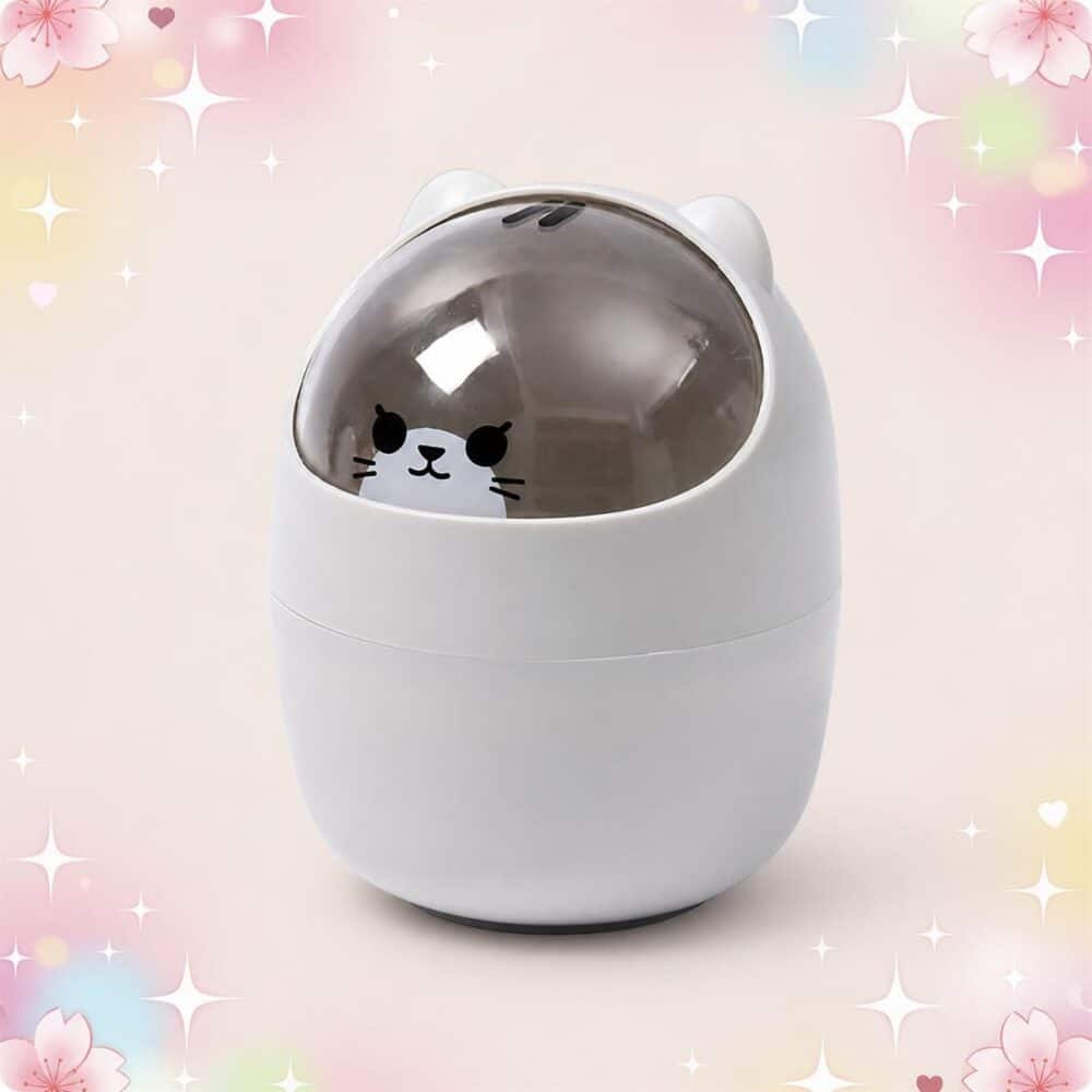Une déco kawaii corbeille de bureau avec tête de chat blanche, en forme d’œuf, avec un petit visage de chat sous un couvercle transparent, sur fond rose pastel avec des cœurs.