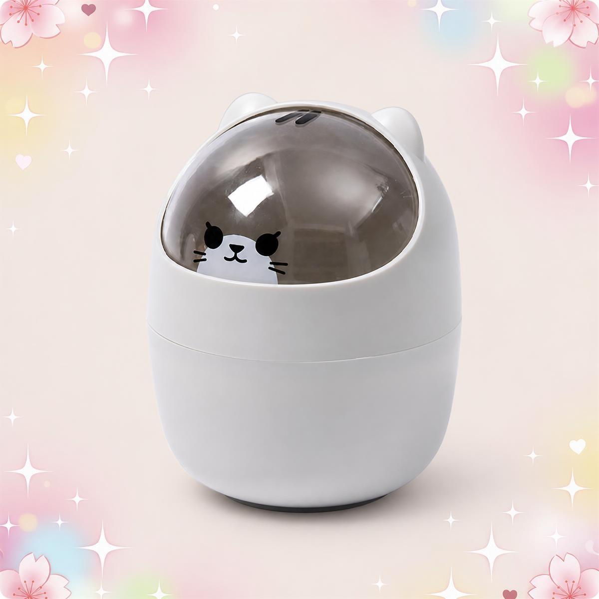 Une déco kawaii corbeille de bureau avec tête de chat blanche, en forme d’œuf, avec un petit visage de chat sous un couvercle transparent, sur fond rose pastel avec des cœurs.