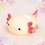 Une déco kawaii petite veilleuse axolotl portable et rechargeable, en forme de petit axolotl rose et crème, sur un fond pastel avec des étoiles et des fleurs.