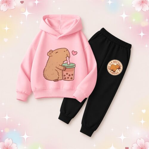 Un enfant portant un ensemble survêtement kawaii capybara bubble tea pour enfant avec un sweat à capuche rose et un pantalon noir, sur fond rose pastel décoré d’étoiles et de fleurs.
