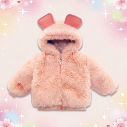 Un manteau à fourrure avec des oreilles pour enfant rose pâle, tout doux, avec capuche et petites oreilles, posé sur un fond pastel décoré de cœurs et d’étoiles.