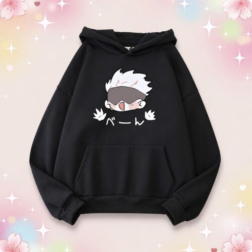 Un pull à capuche oversize kawaii Satoru Gojo noir avec un dessin mignon du personnage, posé sur un fond rose pastel avec des étoiles et des petits cœurs.