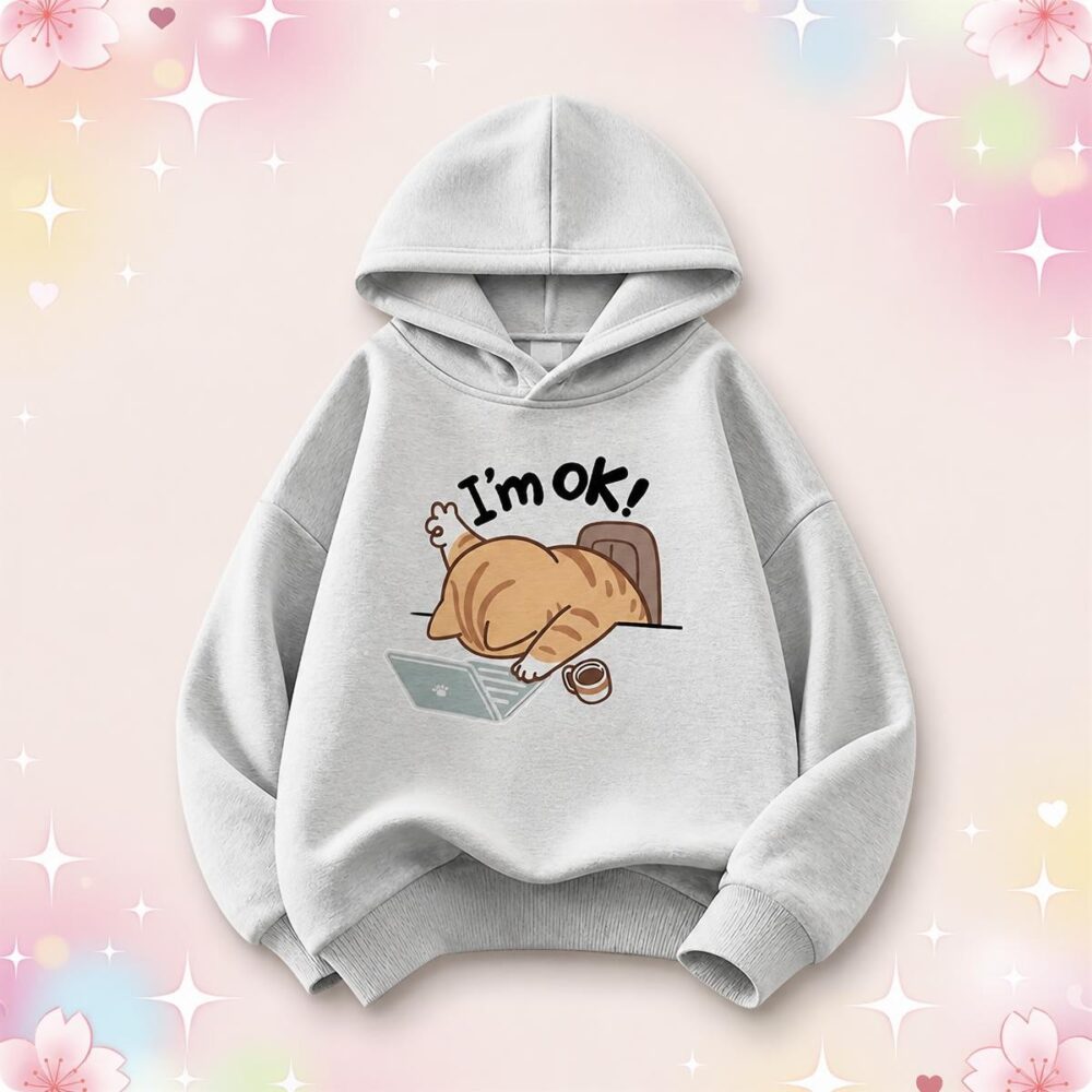 Un pull kawaii pour enfant imprimé chat rigolo gris clair avec un chat endormi et le texte « I'm OK! » sur un fond rose pastel décoré de petits cœurs et d'étoiles.