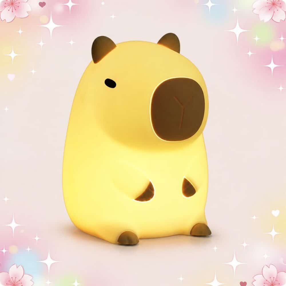 Une déco kawaii lampe veilleuse capybara en forme de petit capybara jaune, avec une lumière douce, sur un fond pastel décoré d’étoiles et de cœurs.