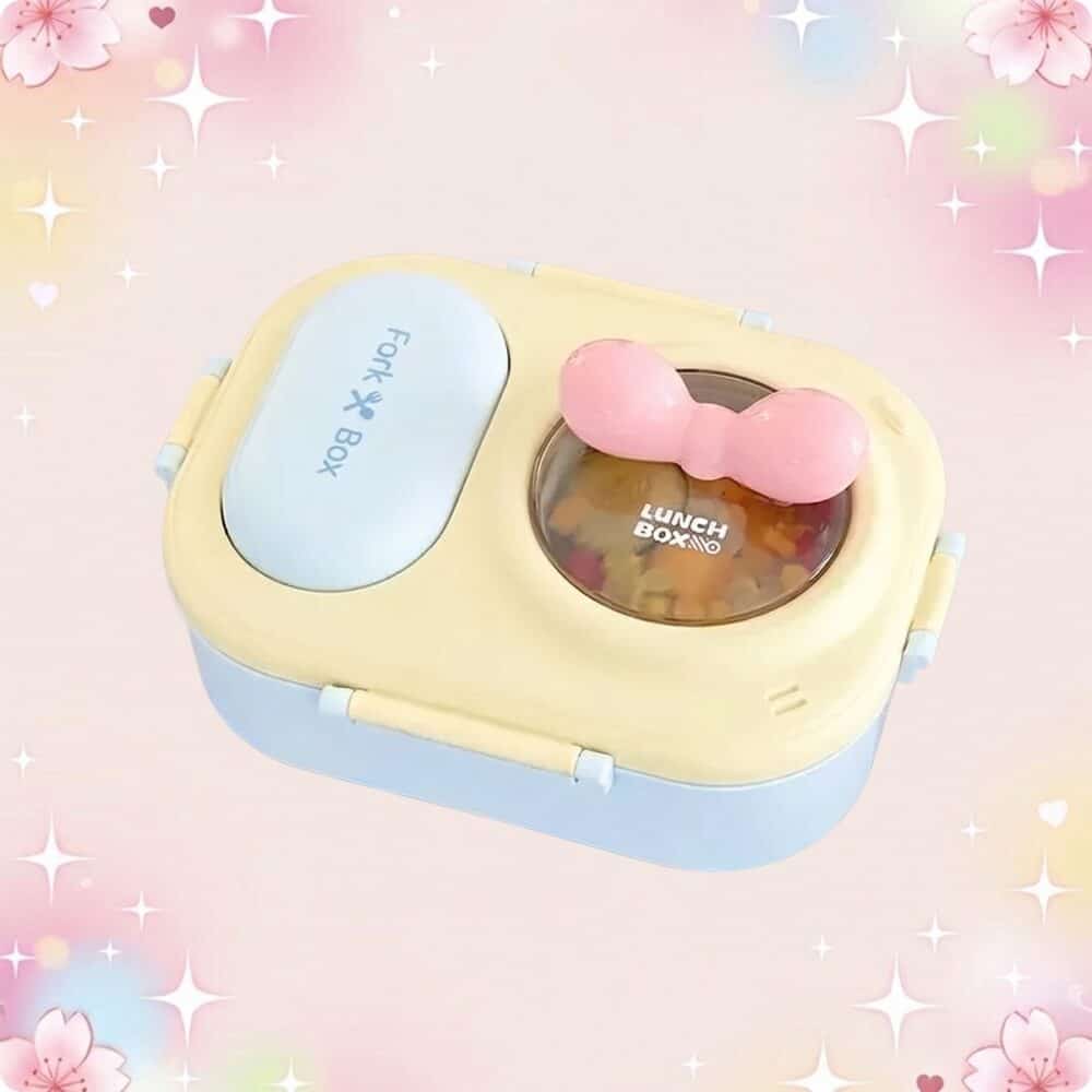 Une lunchbox kawaii à coloris pastel et noeud rose, avec couvercle bleu et jaune, posée sur un fond rose doux et lumineux.