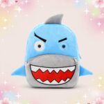 Un sac à dos kawaii requin et son aileron dressé, bleu avec un visage rigolo, une grande bouche aux dents blanches et des nageoires, posé sur un fond pastel décoré d’étoiles et de fleurs.