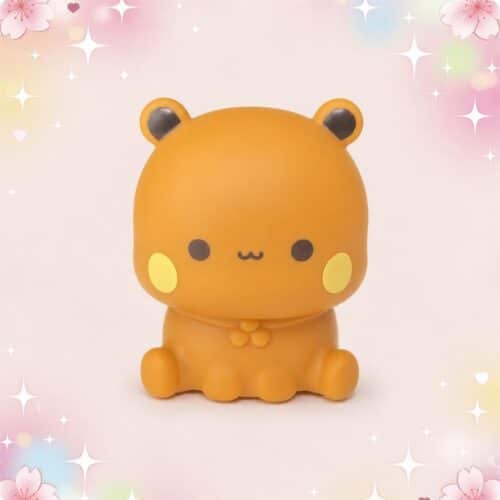 Une veilleuse Kawaii Dudu assis aux joues dorées, en forme de petit animal orange assis, sur un fond rose décoré de fleurs et d’étoiles scintillantes.