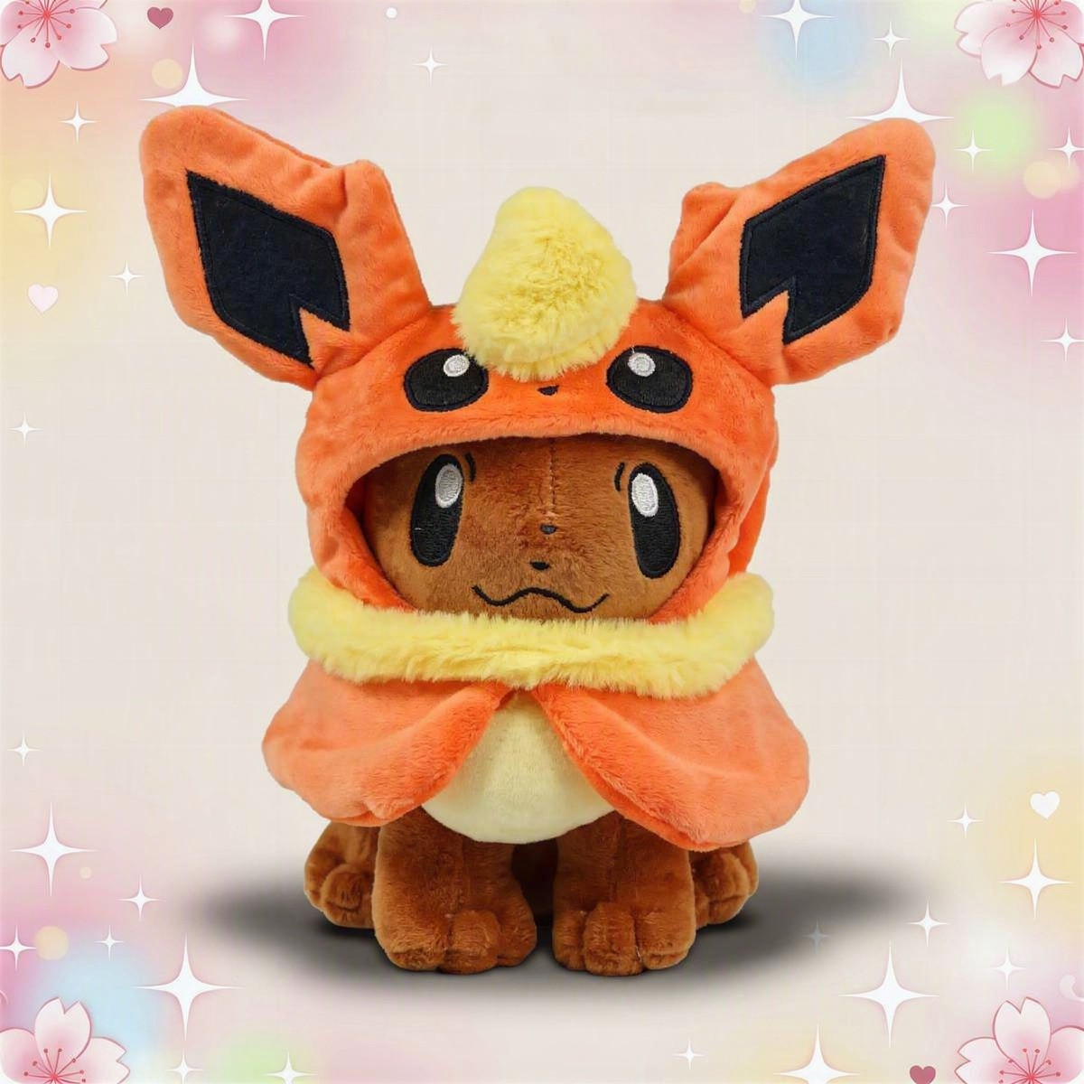 Une peluche Pokémon Evoli déguisé en ses évolutions, vêtue d’un costume orange avec de grandes oreilles et une collerette jaune, posée devant un fond pastel décoré de fleurs et d’étoiles.