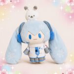 Une peluche Vocaloid Hatsune Miku version snow aux cheveux bleu clair, aux yeux bleus et vêtue d’une tenue blanche et bleue, posée devant un fond pastel décoré d’étoiles et de fleurs.