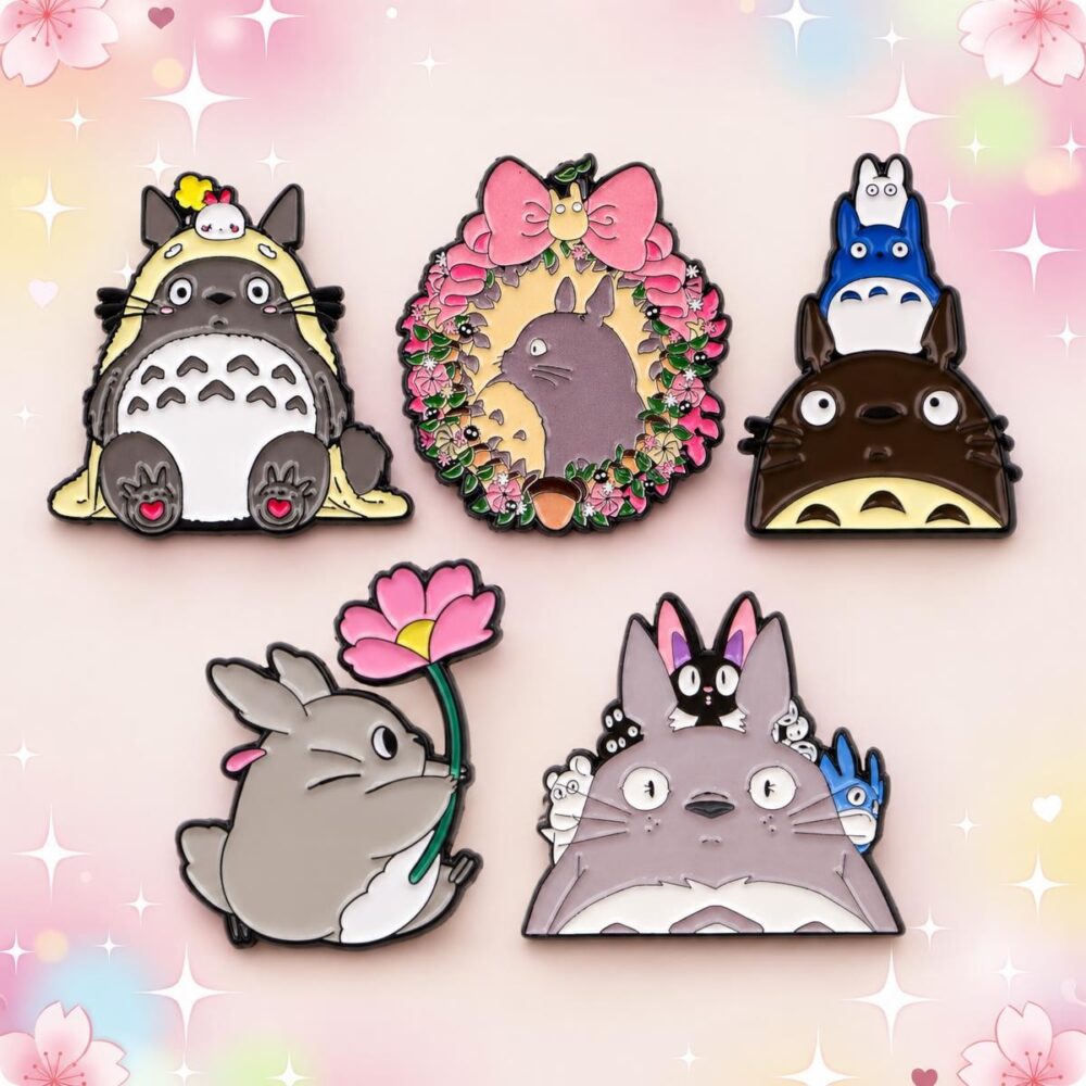 Un lot de 5 pins Kawaii en émail façon Totoro, représentant des personnages et motifs colorés, disposés sur un fond pastel décoré de fleurs et d’étoiles.