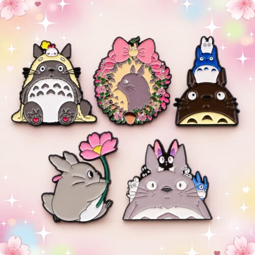 Un lot de 5 pins Kawaii en émail façon Totoro, représentant des personnages et motifs colorés, disposés sur un fond pastel décoré de fleurs et d’étoiles.