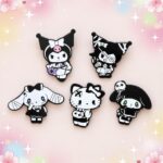 Un lot de 6 pins Kawaii aux personnages de Sanrio style gothique, représentant des personnages en noir et blanc, disposés sur un fond pastel décoré d’étoiles et de fleurs.
